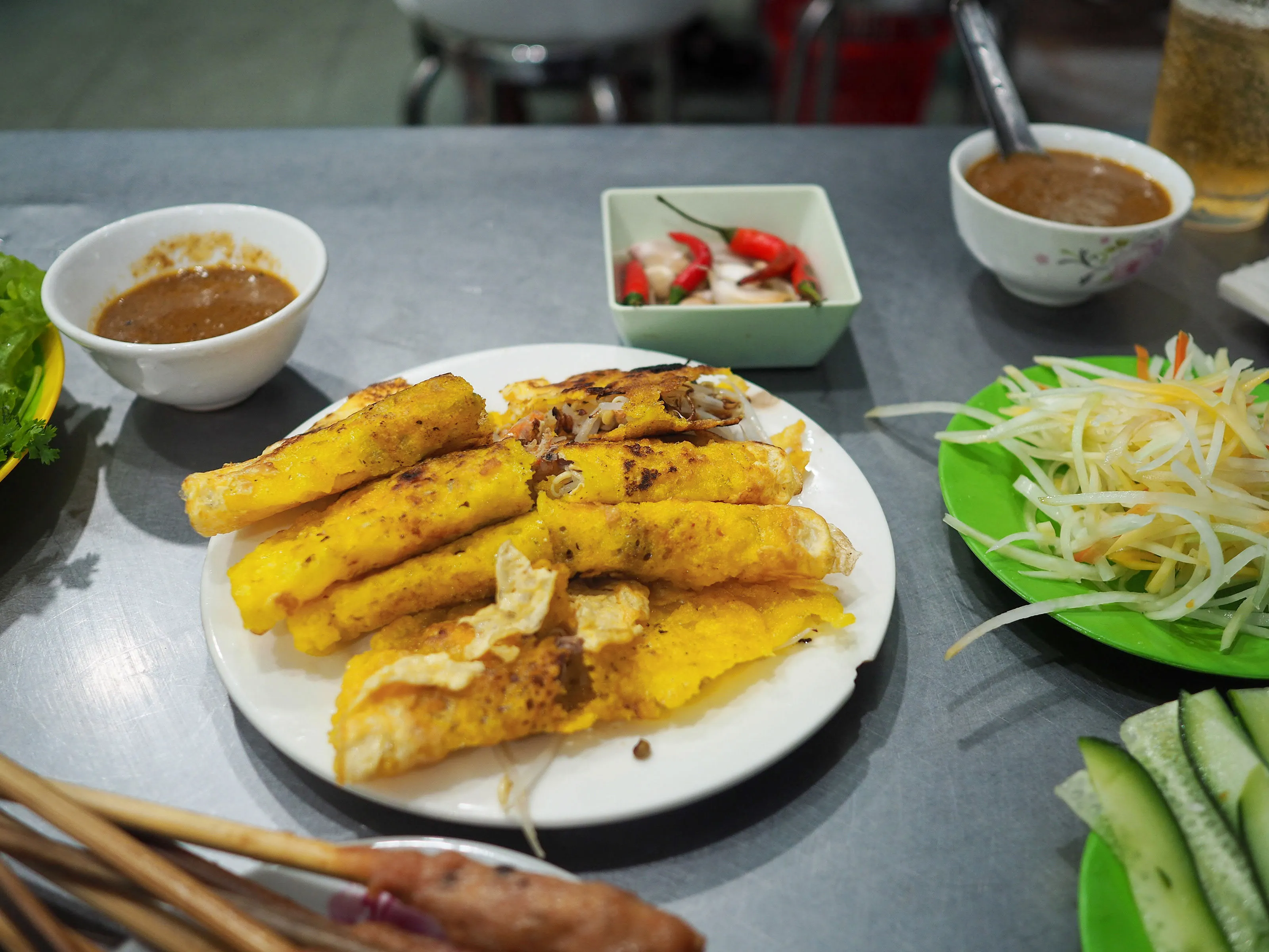 The rice pancakes are crispy fried in a cast iron pan. Tumeric is used to give them a yellow color. Usually, you will find grilled shrimp or squid baked into the pancakes.