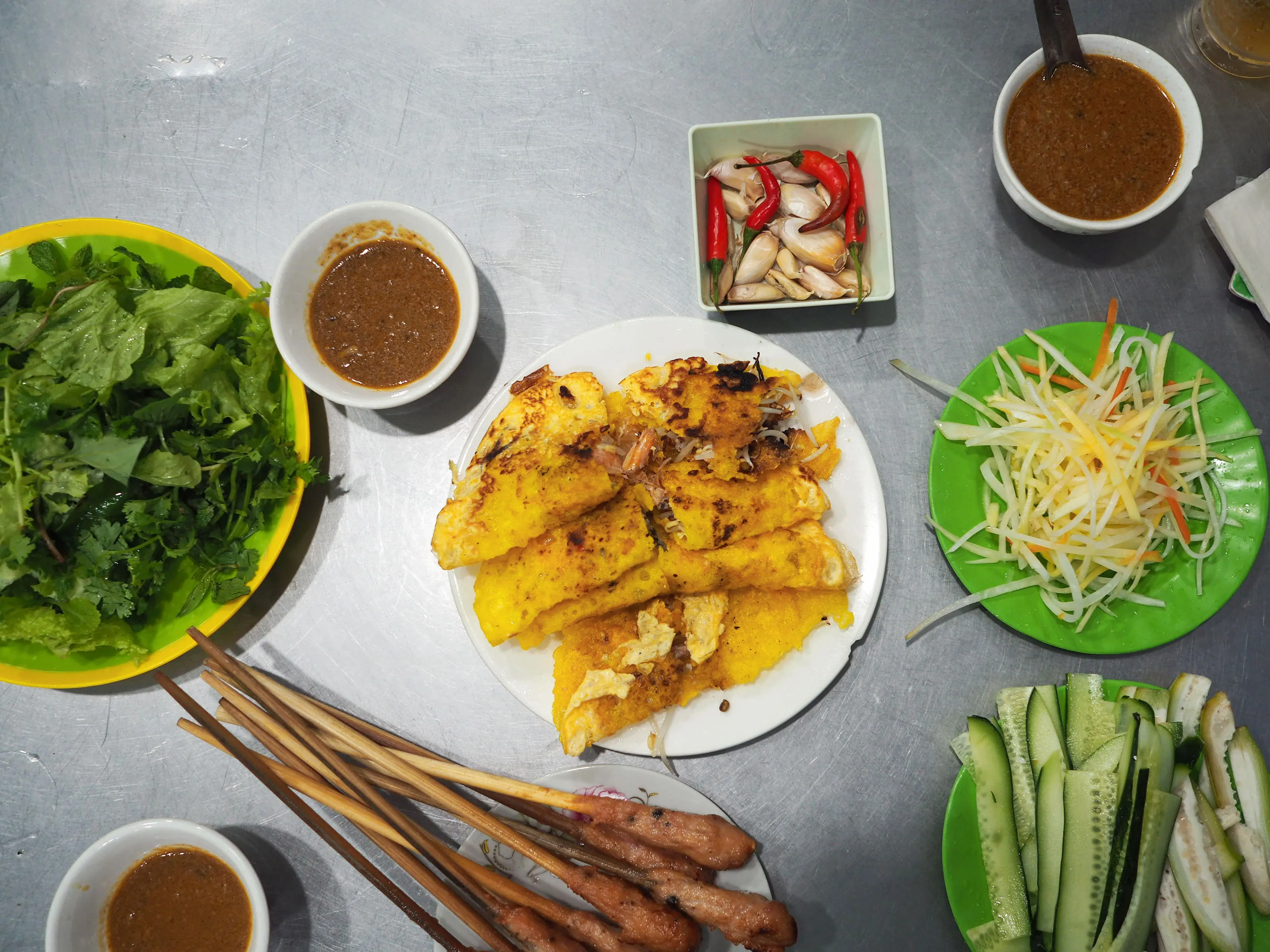 To eat Banh Xeo, you take a piece of rice paper, pile greens, pancake, bean sprouts, ginger, vegetables onto it, pour sauce over it and then roll it into a wrap.